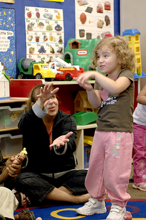 Adult and young child playing a hand game in a classroom